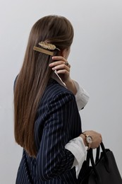 Young woman with beautiful hair clips on light background, back view