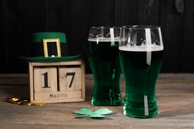 Photo of St. Patrick's day celebrating on March 17. Green beer, block calendar, leprechaun hat, gold coins and decorative clover leaf on wooden table