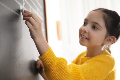 Photo of Little girl writing music notes on blackboard in classroom, closeup