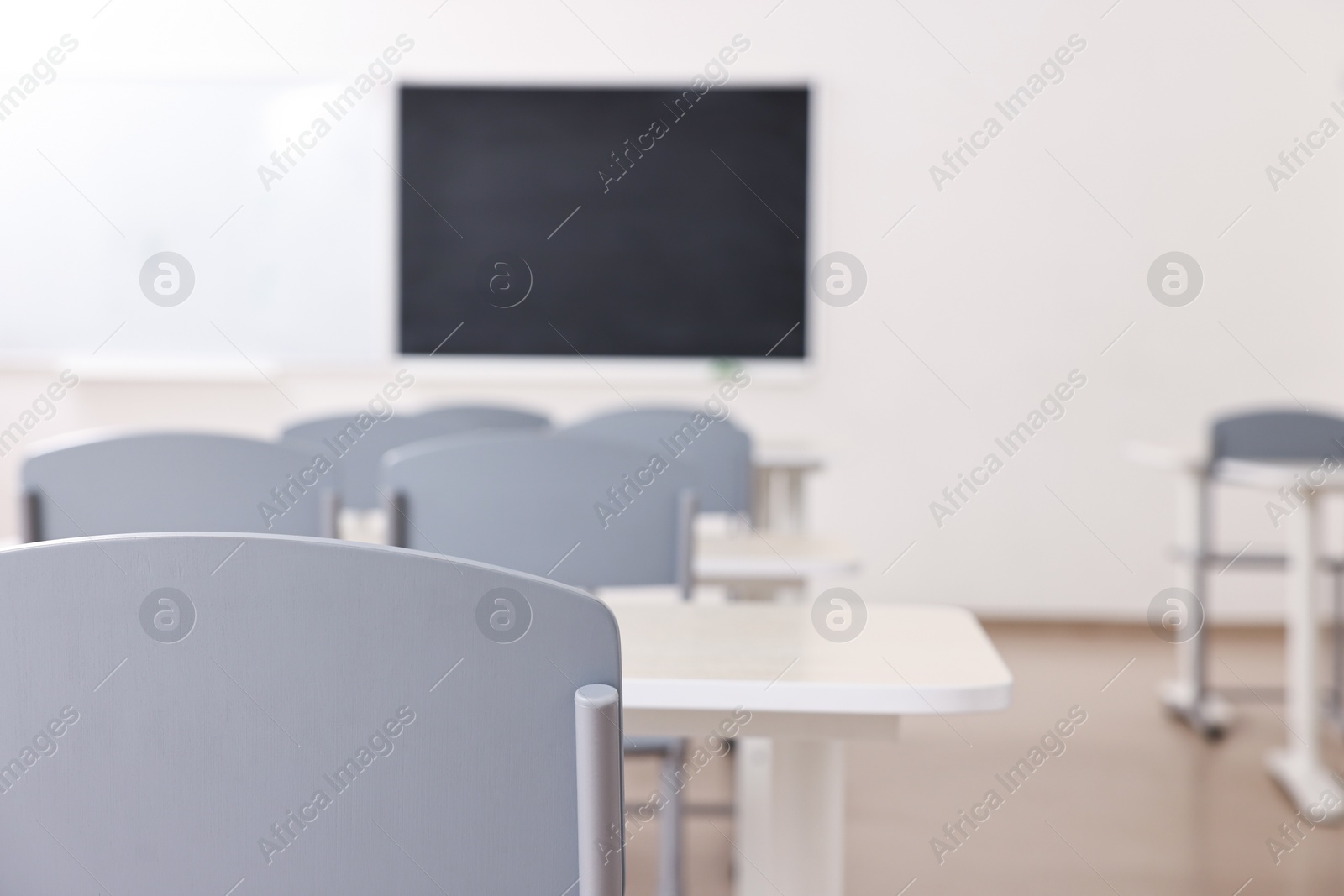 Photo of Empty school classroom with desks, blackboard and chairs