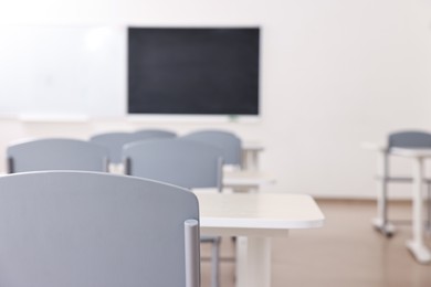 Photo of Empty school classroom with desks, blackboard and chairs