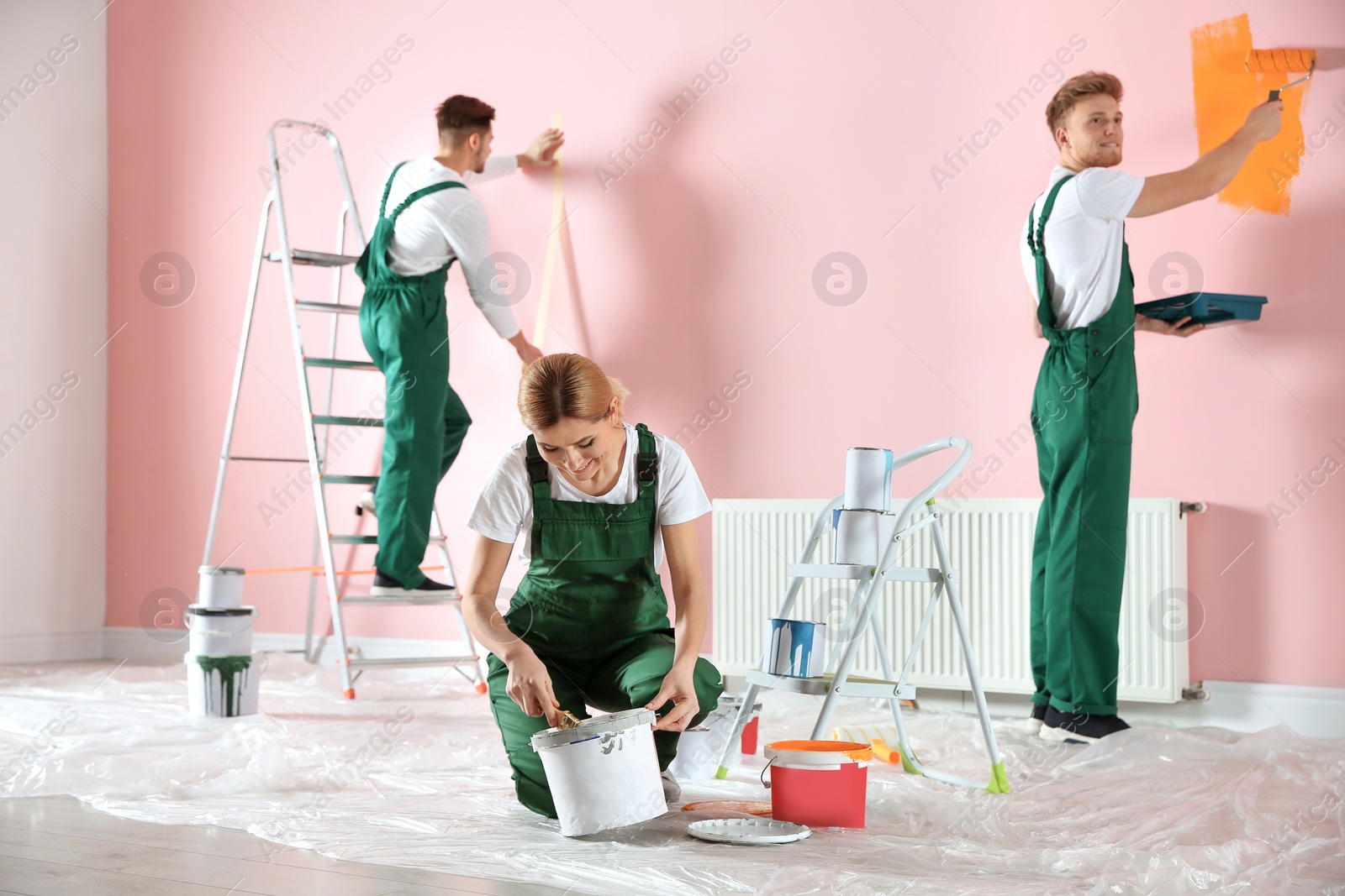 Photo of Team of professional decorators painting wall indoors. Home repair service