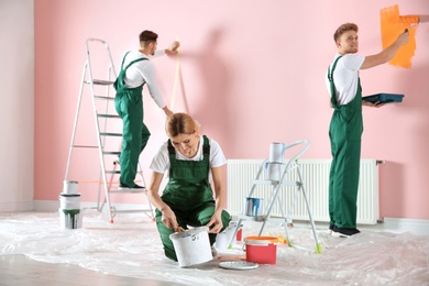 Photo of Team of professional decorators painting wall indoors. Home repair service