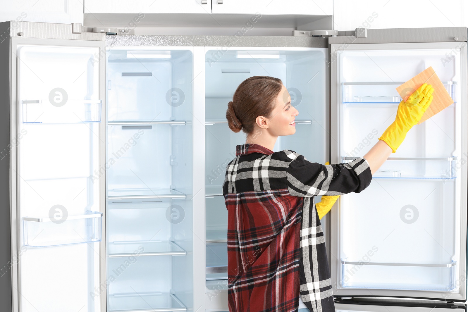 Photo of Woman in rubber gloves cleaning refrigerator at home