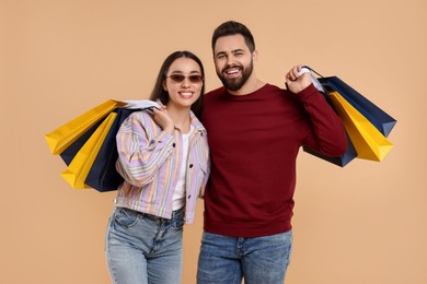 Happy couple with shopping bags on beige background