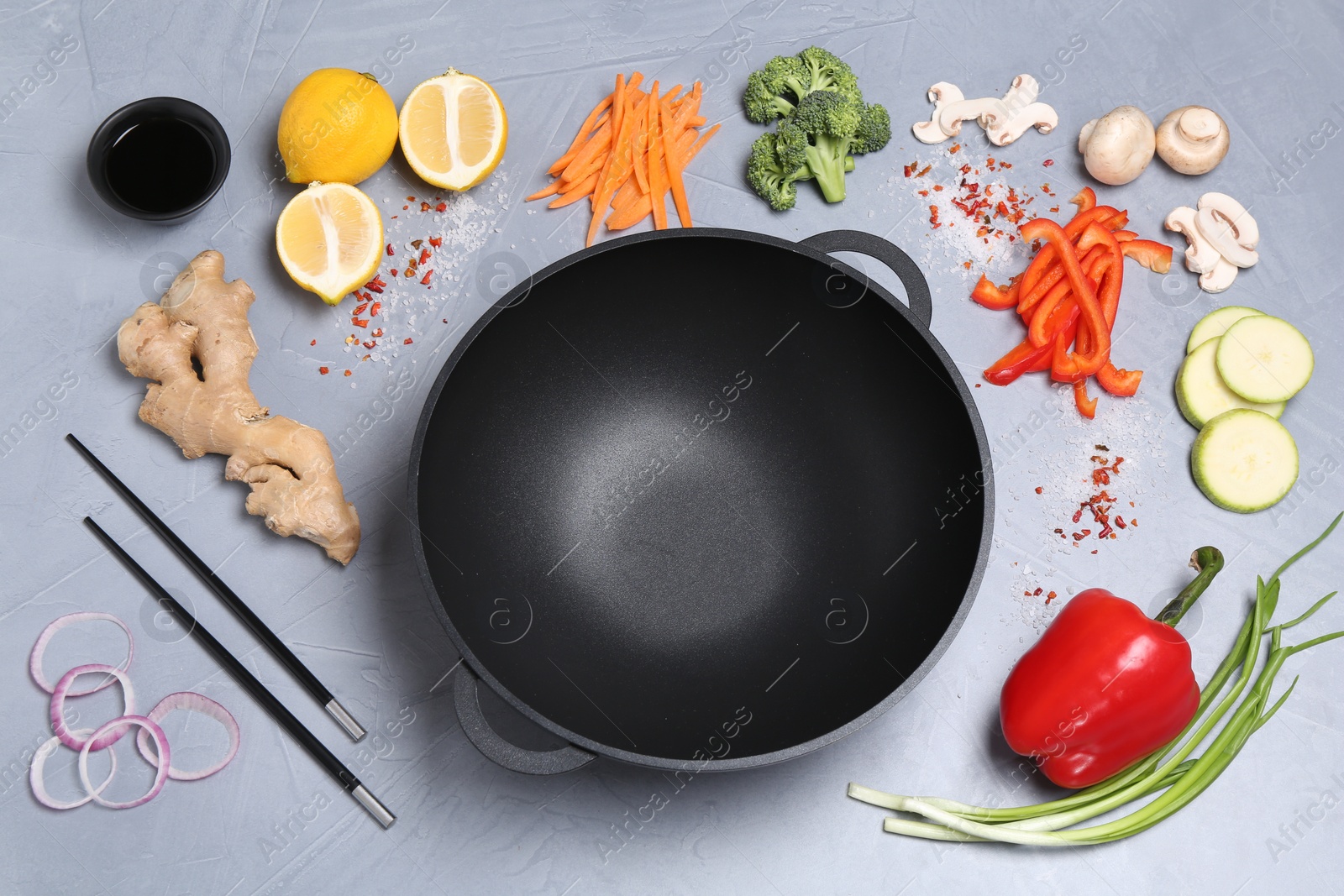 Photo of Wok, chopsticks and different products on grey table, above view