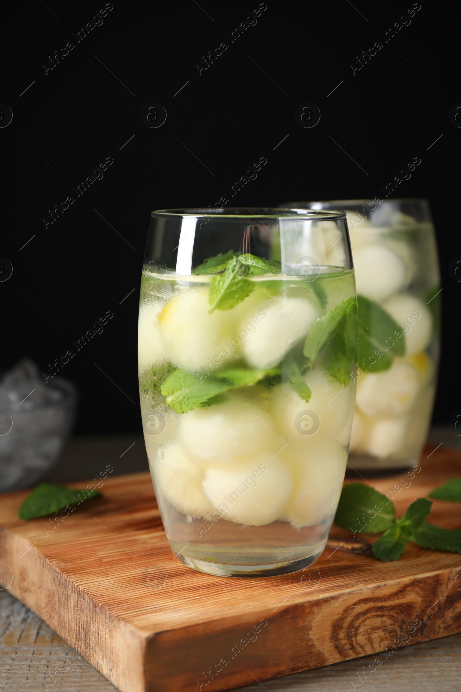 Photo of Tasty melon ball drink on wooden table against black background