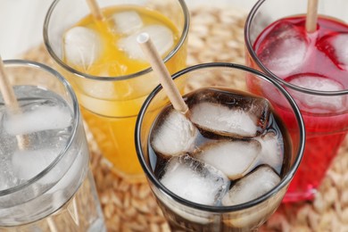 Photo of Glasses of different refreshing soda water with ice cubes and straws on wicker mat, closeup