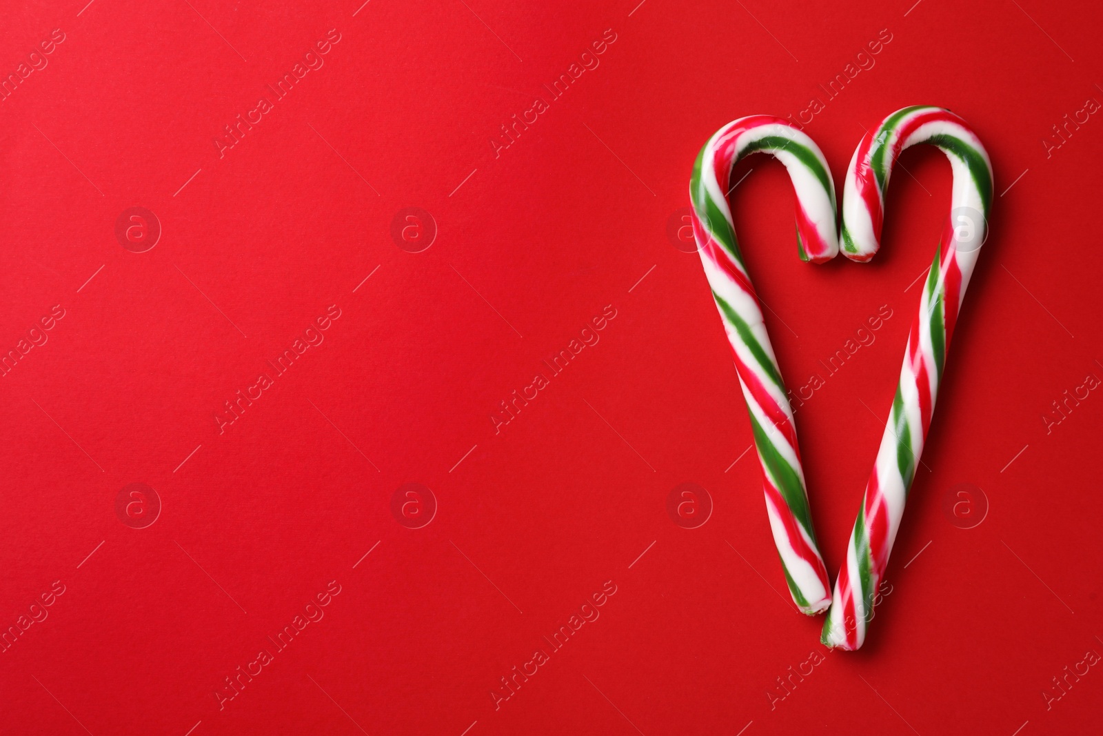 Photo of Heart made of Christmas candy canes on red background, flat lay. Space for text