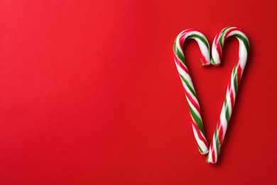 Heart made of Christmas candy canes on red background, flat lay. Space for text