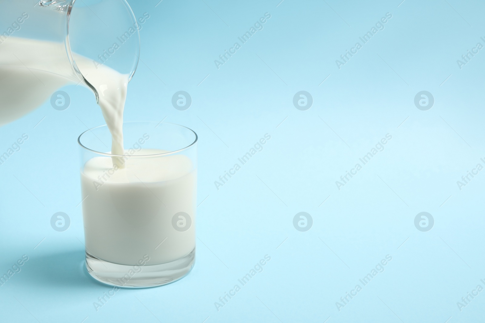 Photo of Pouring milk into glass on light blue background. Space for text