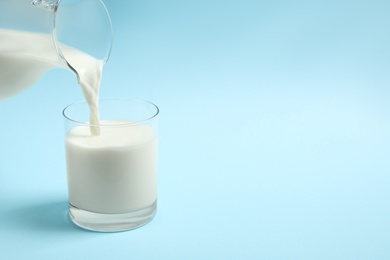 Photo of Pouring milk into glass on light blue background. Space for text