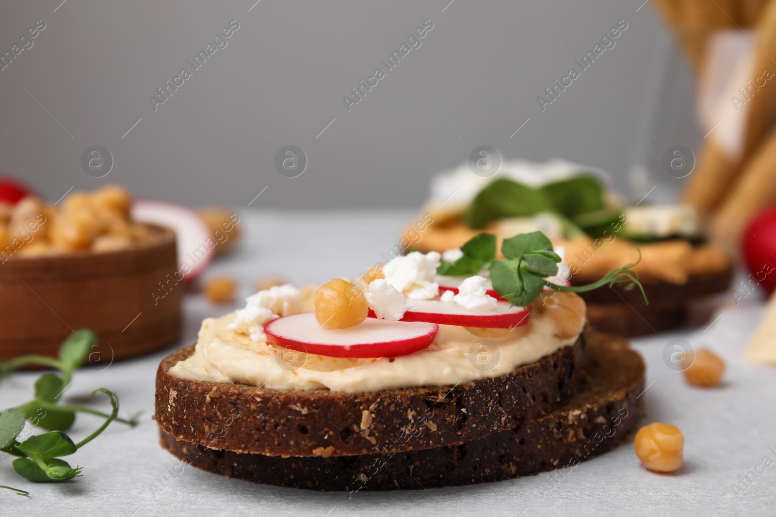 Photo of Delicious sandwiches with hummus and ingredients on light grey table, closeup