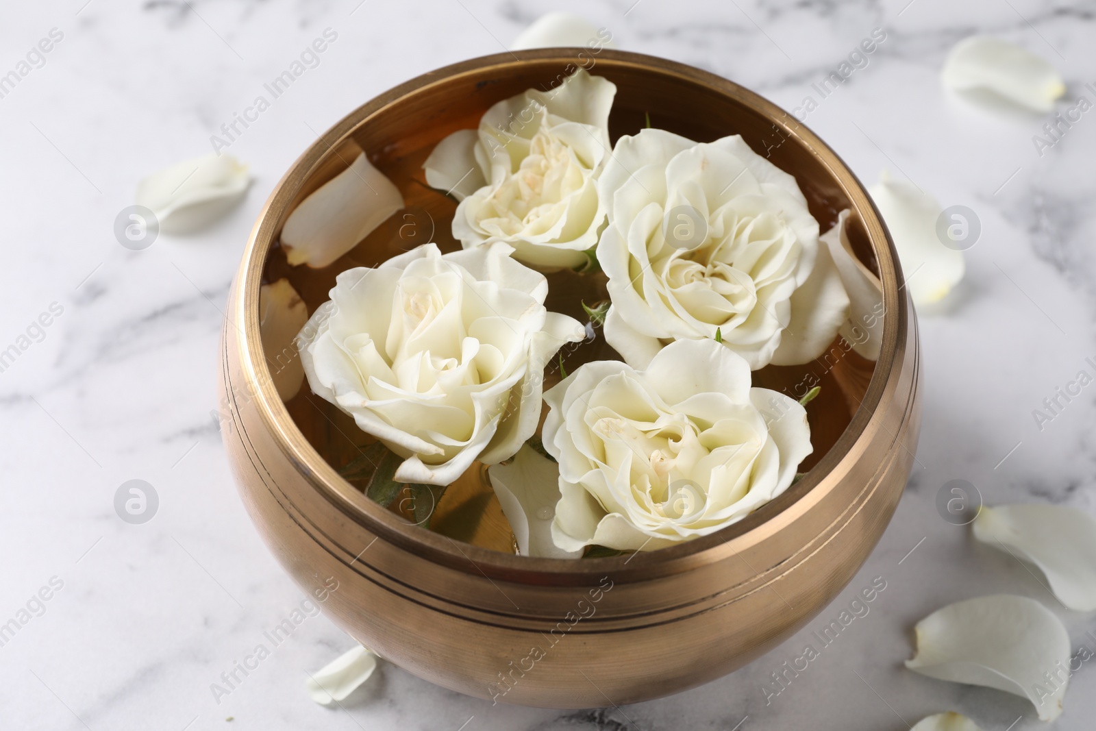 Photo of Tibetan singing bowl with water and beautiful roses on white marble table, closeup