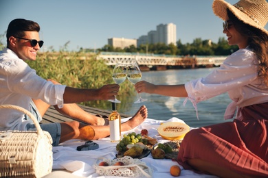 Photo of Couple clinking glasses with wine on pier at picnic