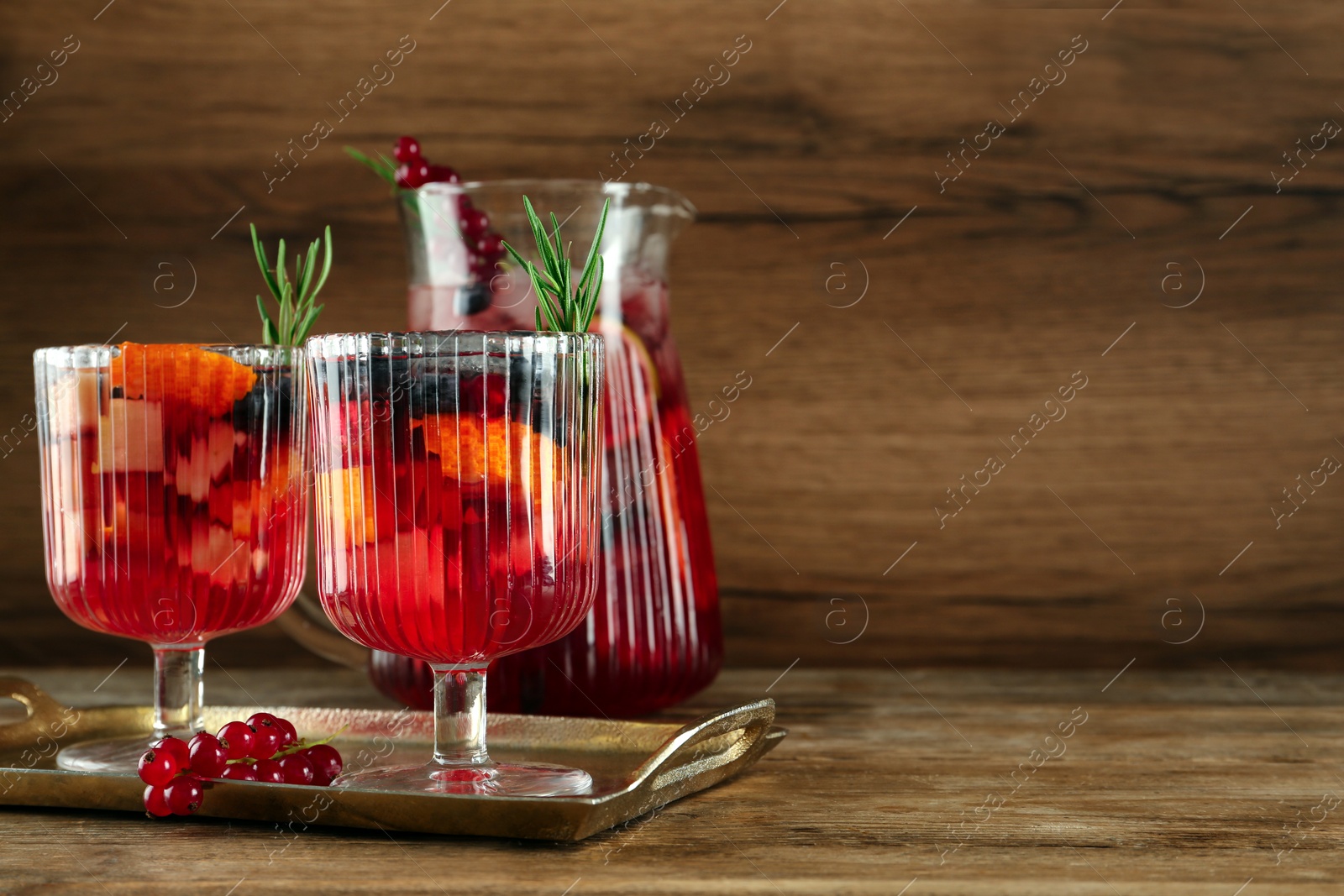 Photo of Glasses and jug of Red Sangria on wooden table. Space for text