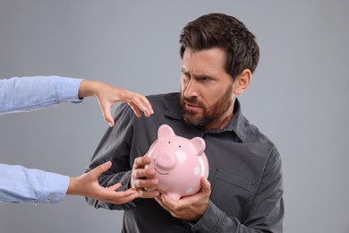 Man trying to protect piggy bank from woman on light grey background. Be careful - fraud