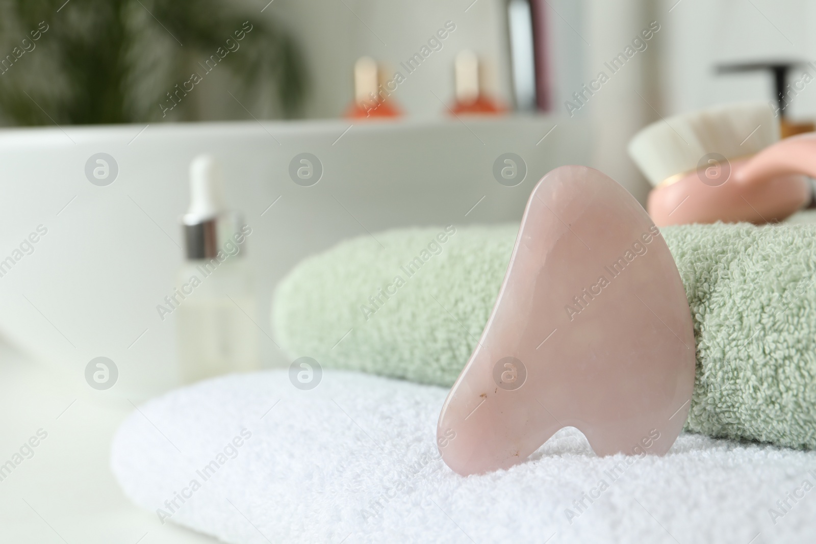 Photo of Rose quartz gua sha tool with soft towels on table in bathroom, closeup. Space for text