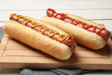 Photo of Delicious hot dogs with mustard and ketchup on wooden board, closeup