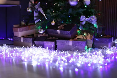 Photo of Beautiful Christmas tree, fairy lights and gift boxes indoors