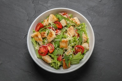 Photo of Delicious fresh Caesar salad on black table, top view