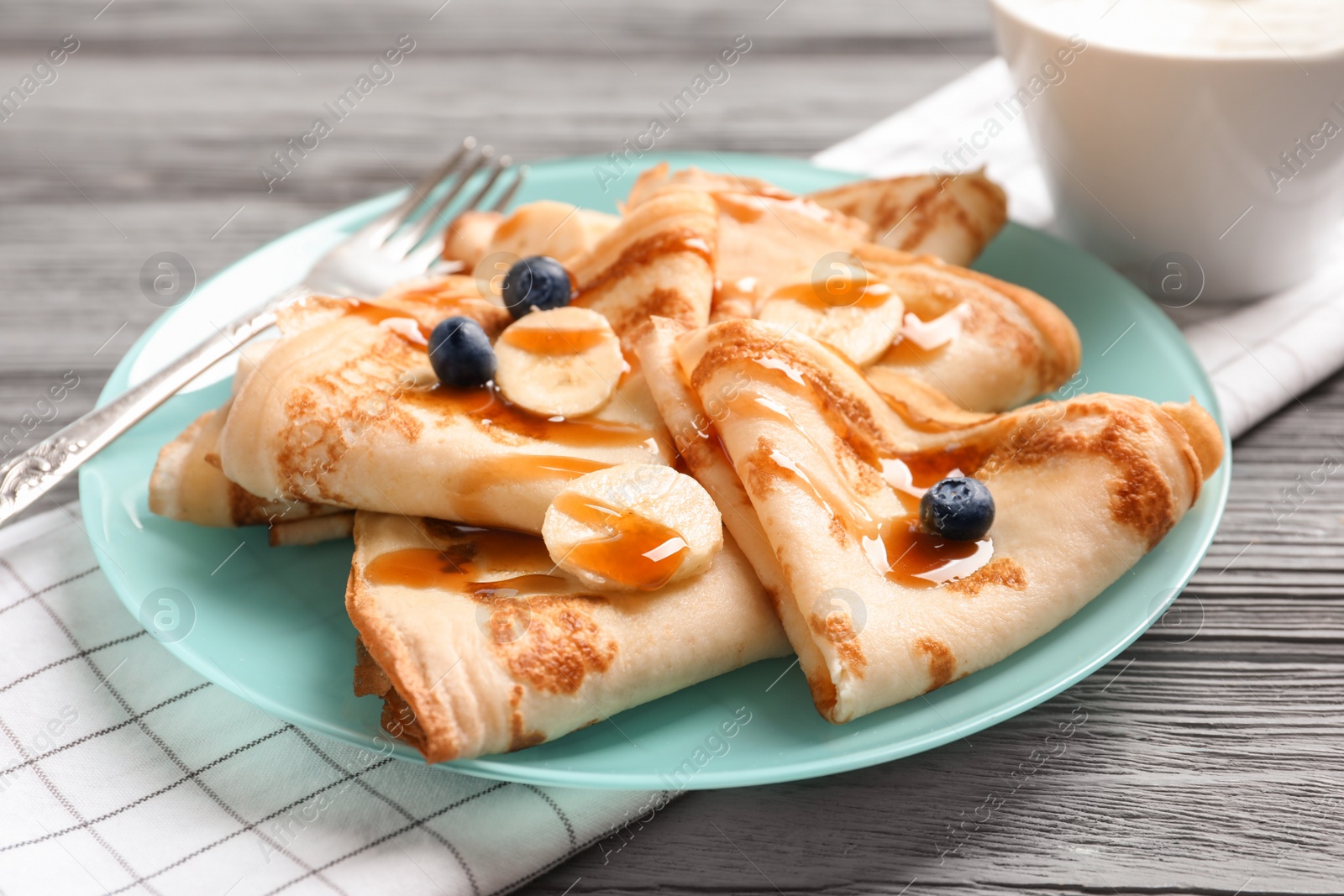 Photo of Thin pancakes served with syrup, berries and banana on plate