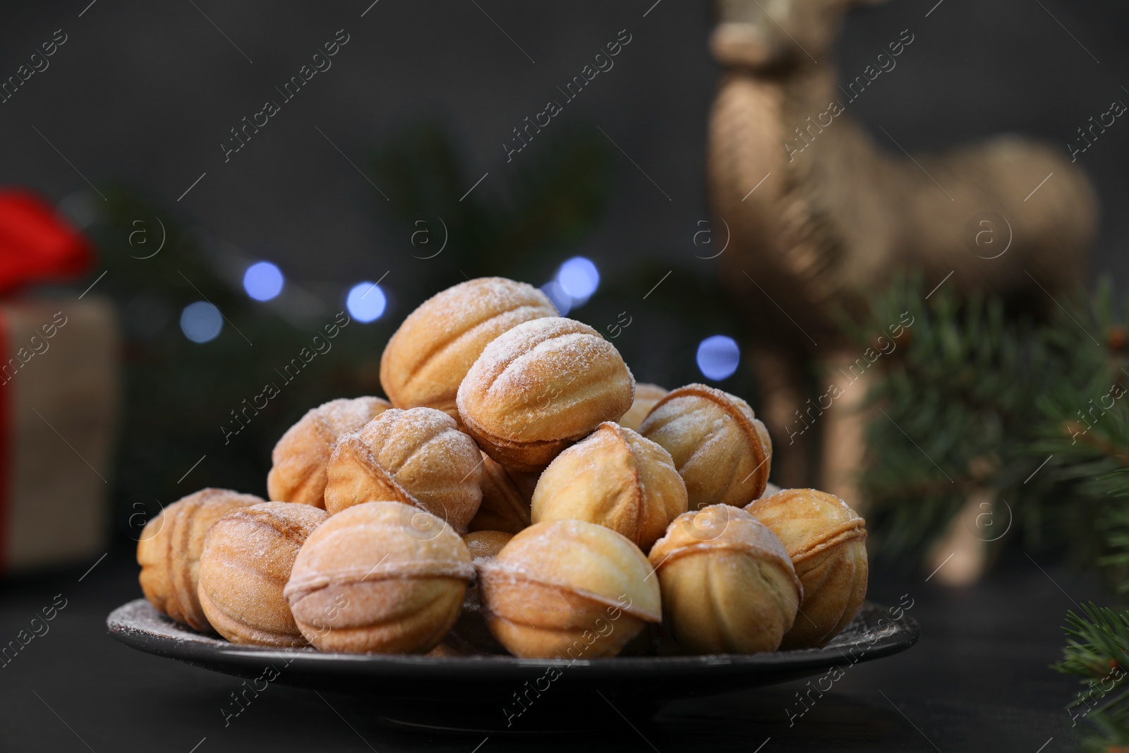 Photo of Plate of tasty nut shaped cookies with powdered sugar on black table, closeup