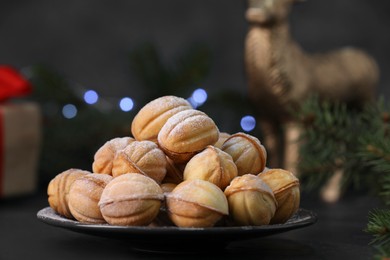 Plate of tasty nut shaped cookies with powdered sugar on black table, closeup