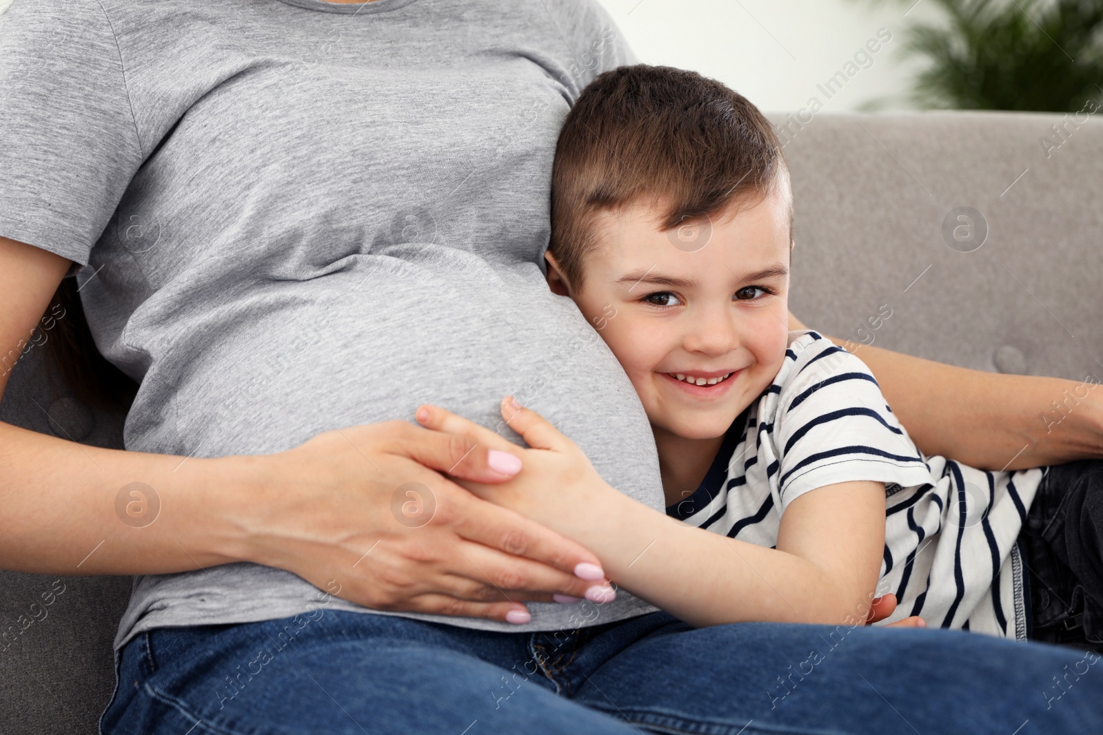 Photo of Pregnant mother and son sitting together on sofa at home, closeup