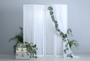 Photo of Stylish photo zone with white folding screen, floral decor and vintage suitcases indoors