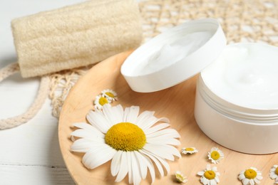 Jar of cream and chamomiles on wooden plate, closeup