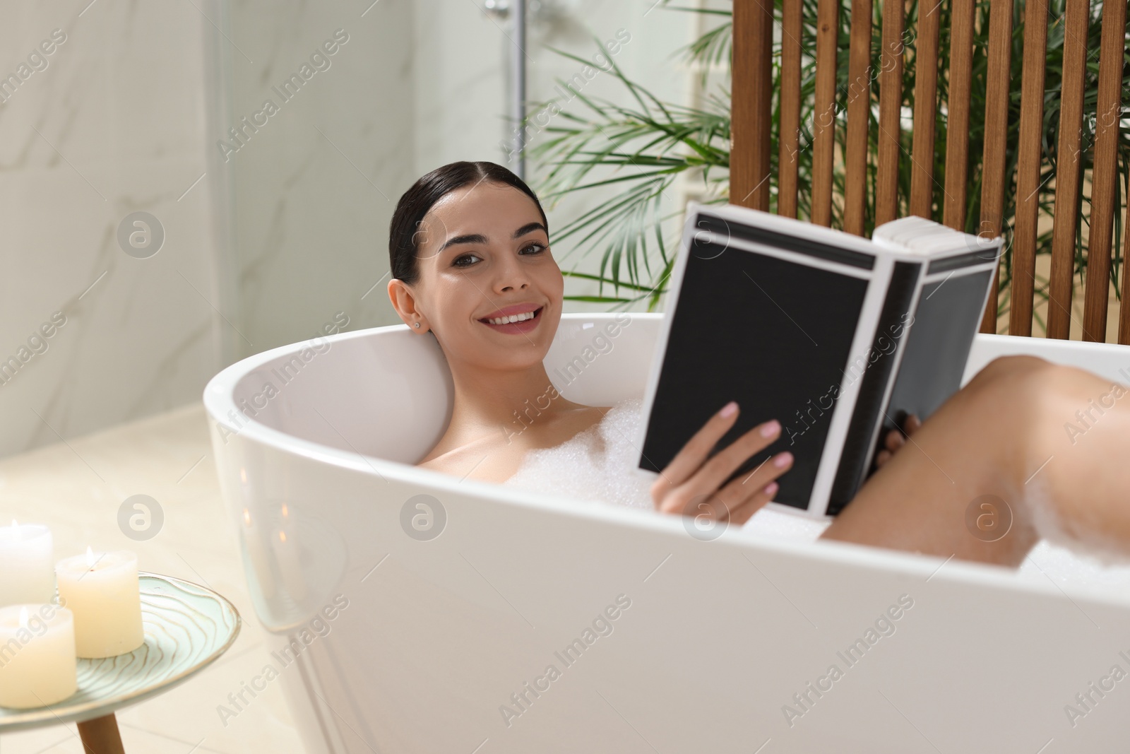 Photo of Beautiful young woman reading book while taking bath at home