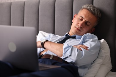 Businessman with laptop sleeping on bed indoors