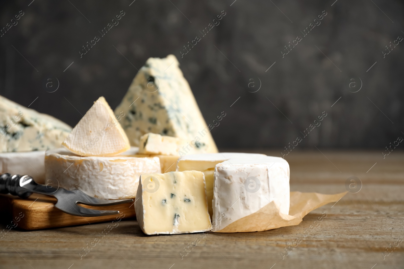 Photo of Different sorts of cheese and fork on wooden table, closeup. Space for text