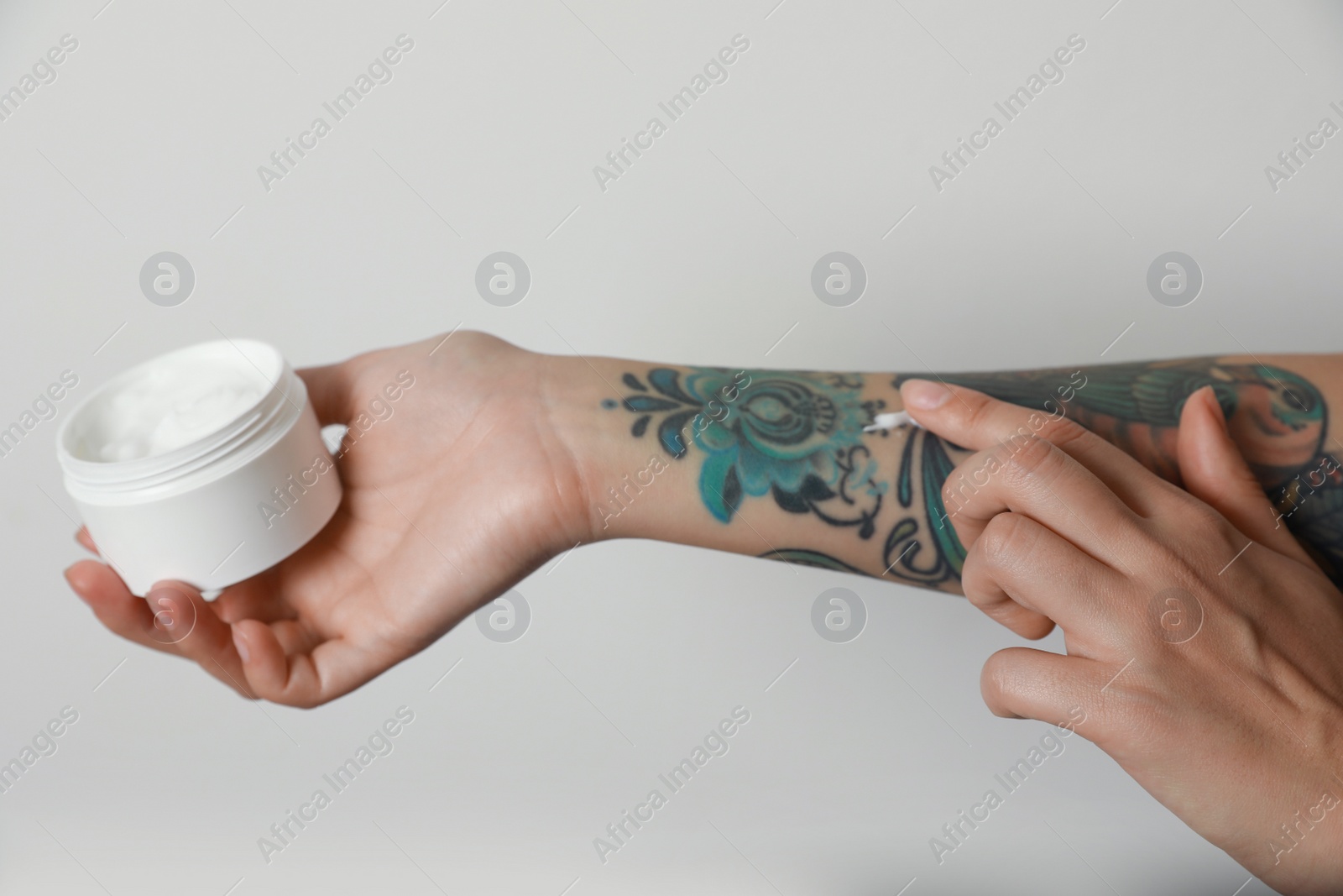 Photo of Woman applying cream on her arm with tattoos against light background, closeup