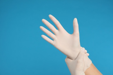 Doctor wearing medical gloves on light blue background, closeup