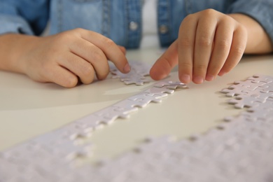 Photo of Little girl playing with puzzles at table, closeup
