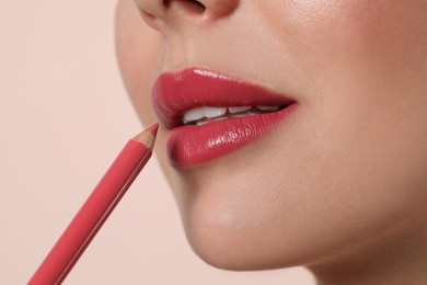 Young woman applying beautiful pink lip pencil on light background, closeup