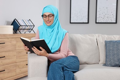 Muslim woman reading book on couch in room. Space for text