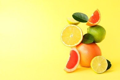 Photo of Fresh ripe citrus fruits and green leaves on yellow background, space for text