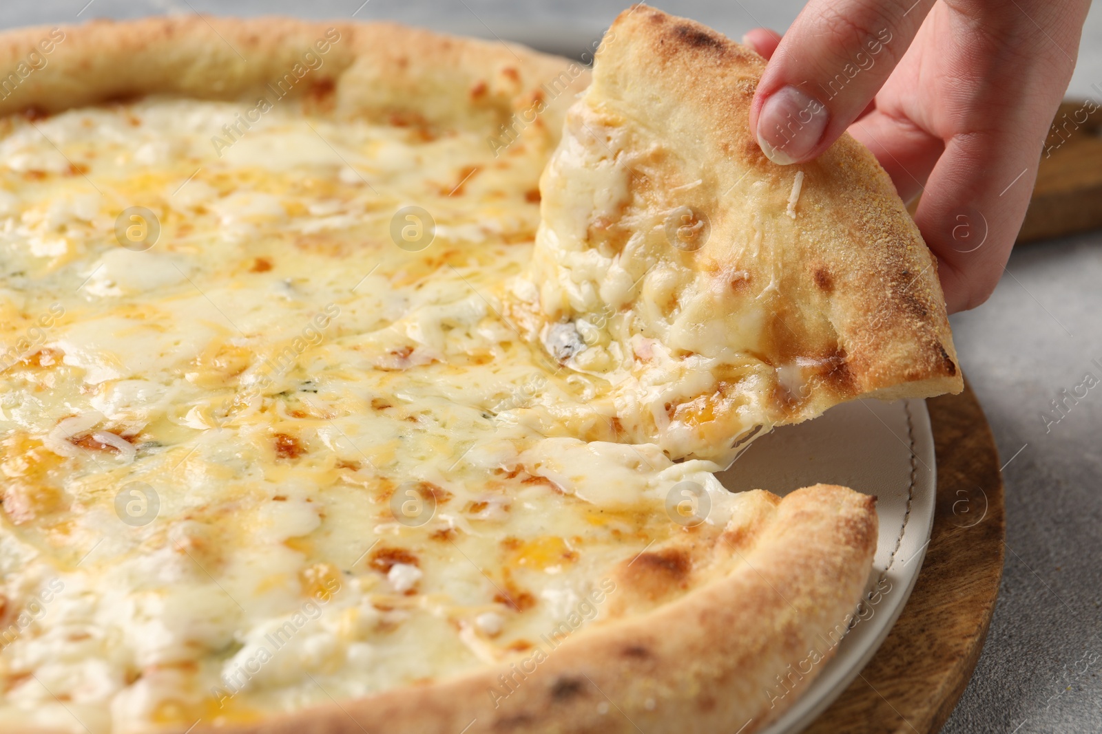 Photo of Woman taking piece of delicious cheese pizza at light grey table, closeup