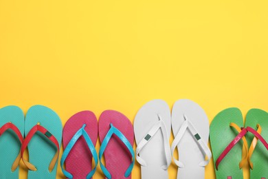 Many different stylish flip flops on yellow background, flat lay. Space for text