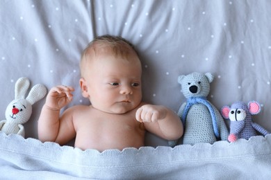 Cute newborn baby with toys in bed, top view
