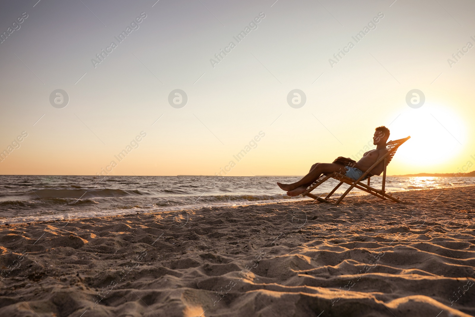 Photo of Young man reading book in deck chair on beach