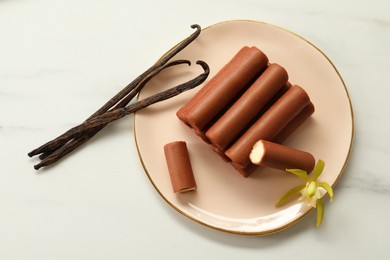 Photo of Glazed curd cheese bars, vanilla pods and flower on white marble table, top view