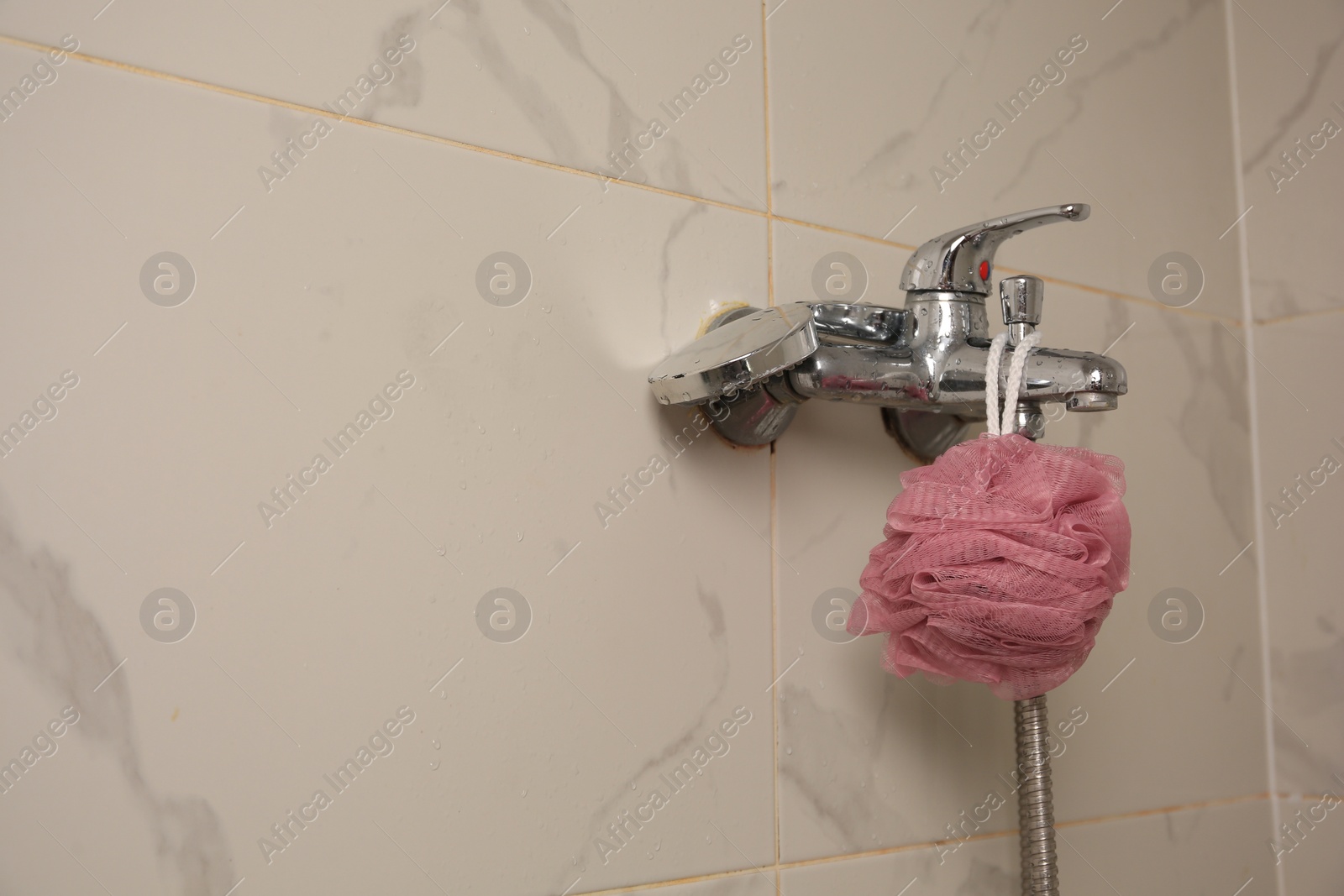 Photo of Pink shower puff hanging on faucet in bathroom, space for text