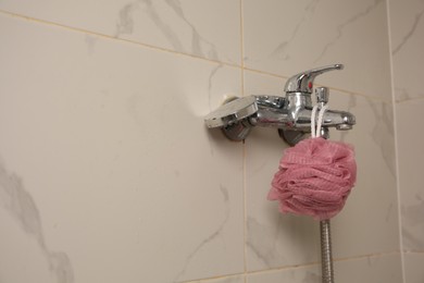 Photo of Pink shower puff hanging on faucet in bathroom, space for text