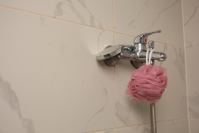 Pink shower puff hanging on faucet in bathroom, space for text