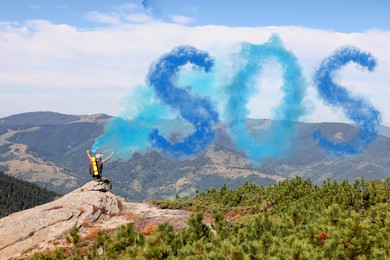 Image of Man with backpack and word SOS made of color smoke bomb on rocky peak in mountains, back view