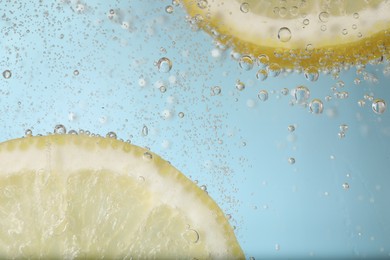 Photo of Juicy lemon slices in soda water against light blue background, closeup